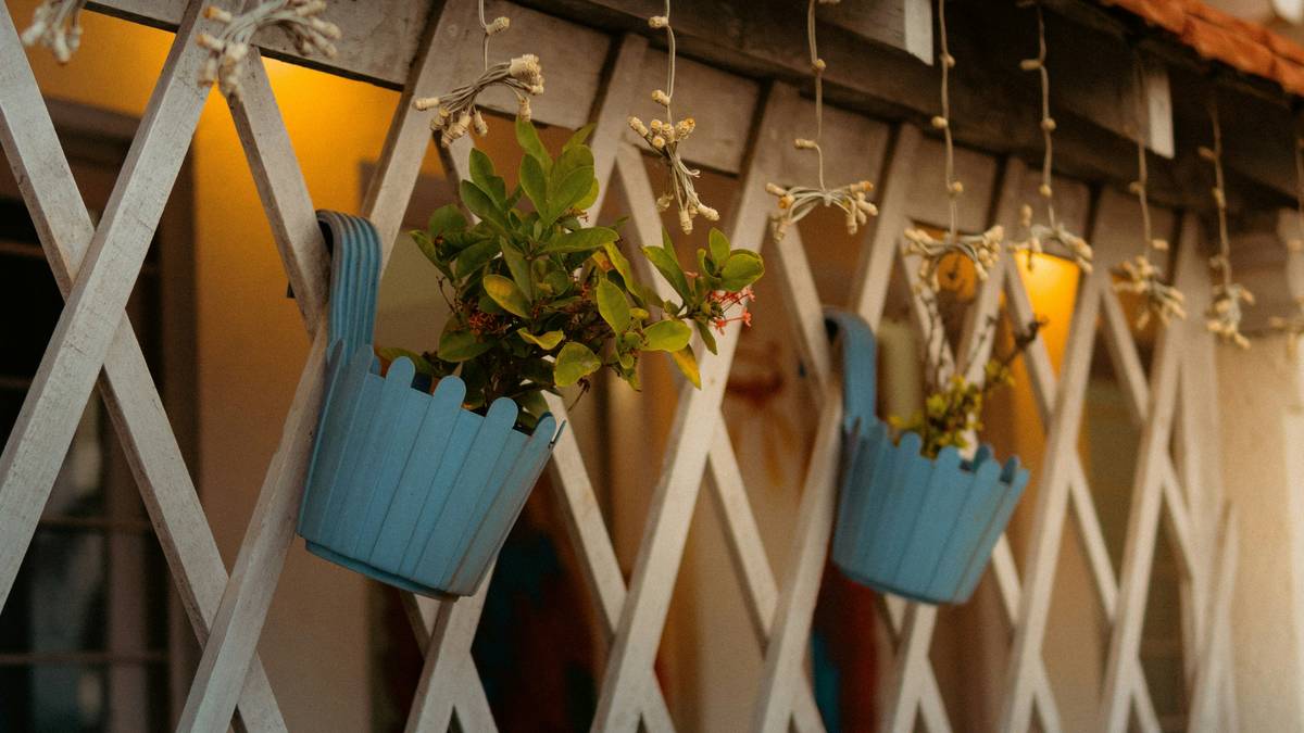 Decorative hanging garden ornaments including glass suncatchers, metal wind spirals, and ceramic birds suspended from a wooden pergola beam